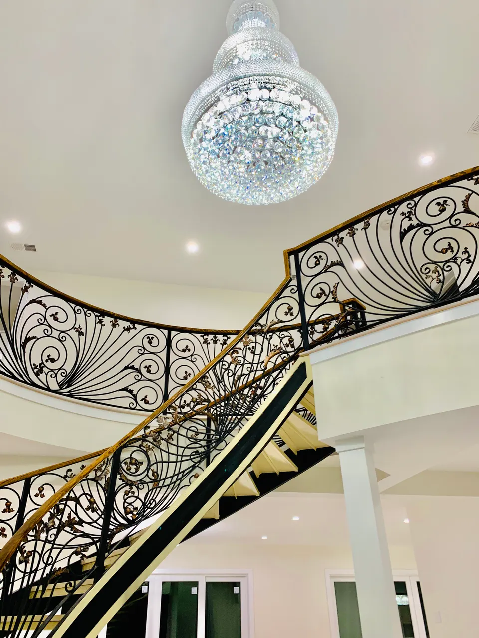 Ornamental curved balustrade with gold-toned handrail below a crystal chandelier