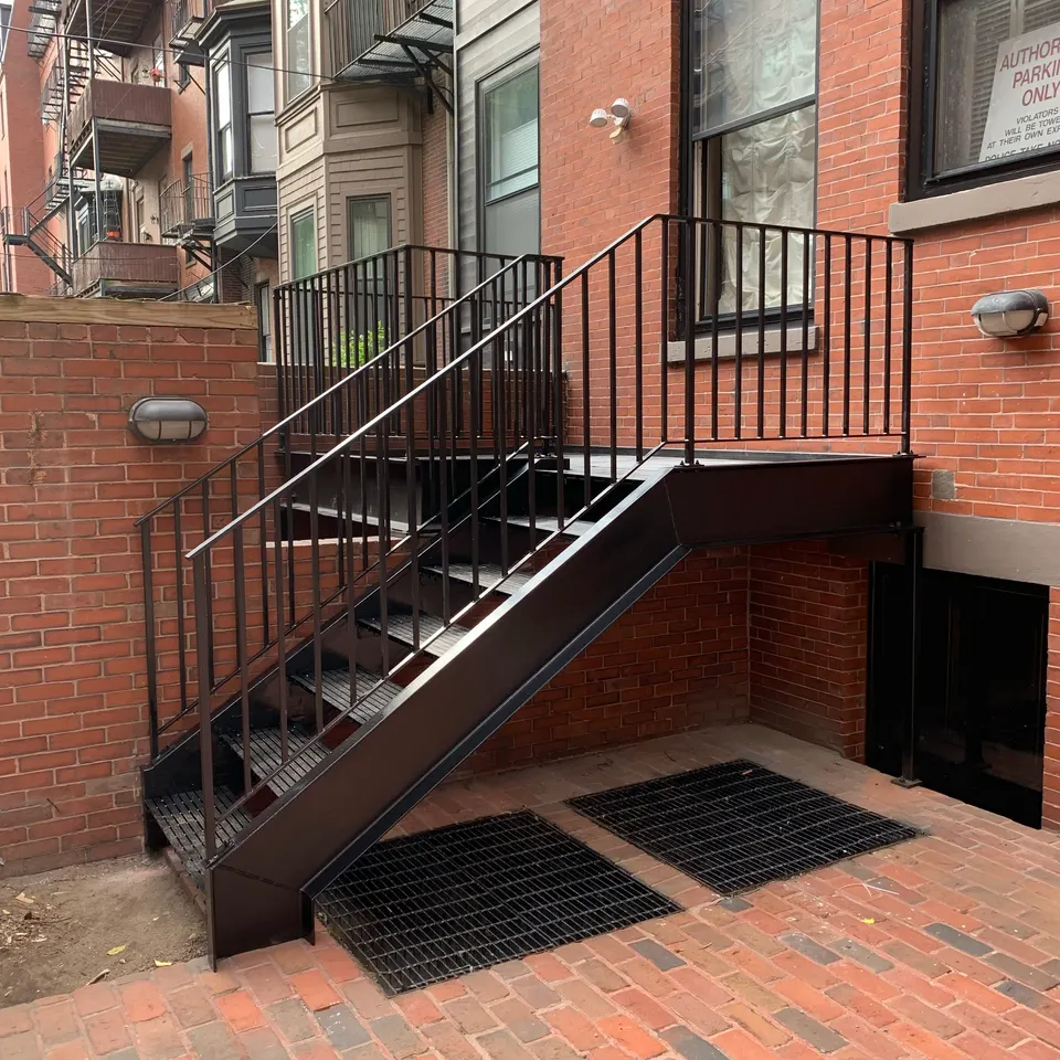 Black steel stair with picket railings leading down beside a brick wall