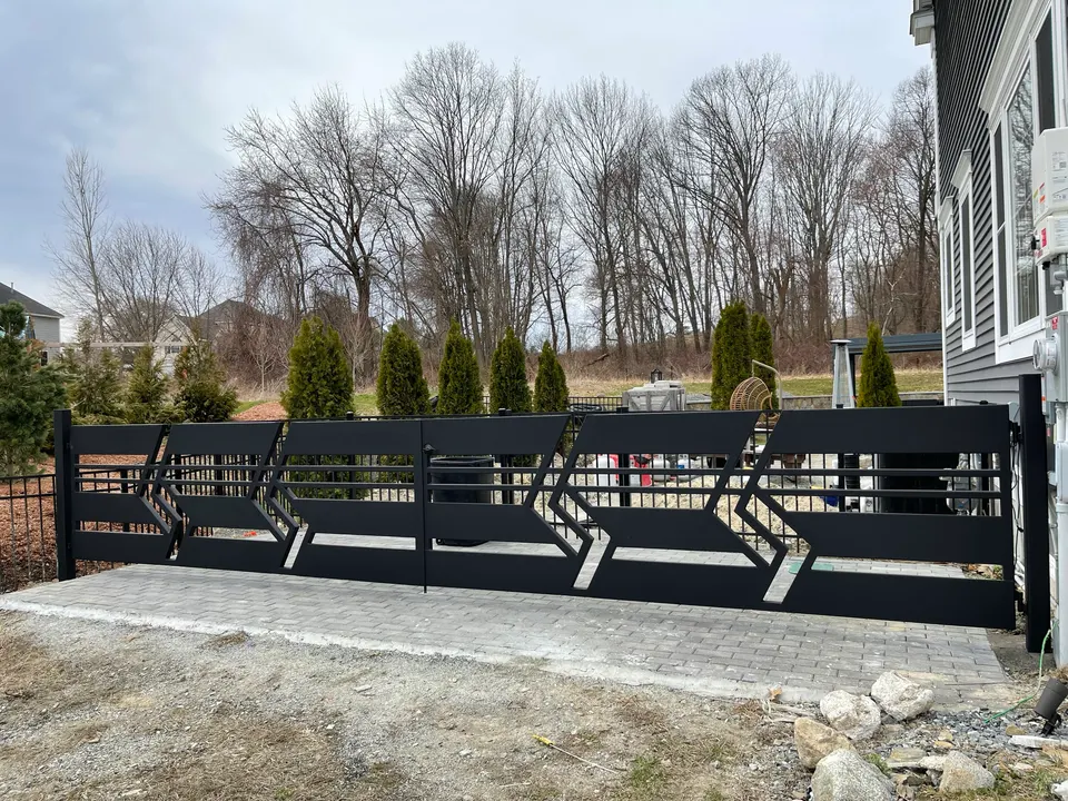 Black fence with geometric chevron panels along a new paver patio