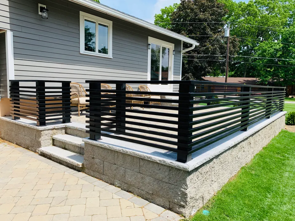 Black horizontal-bar fence panels on a stone base beside a paver patio