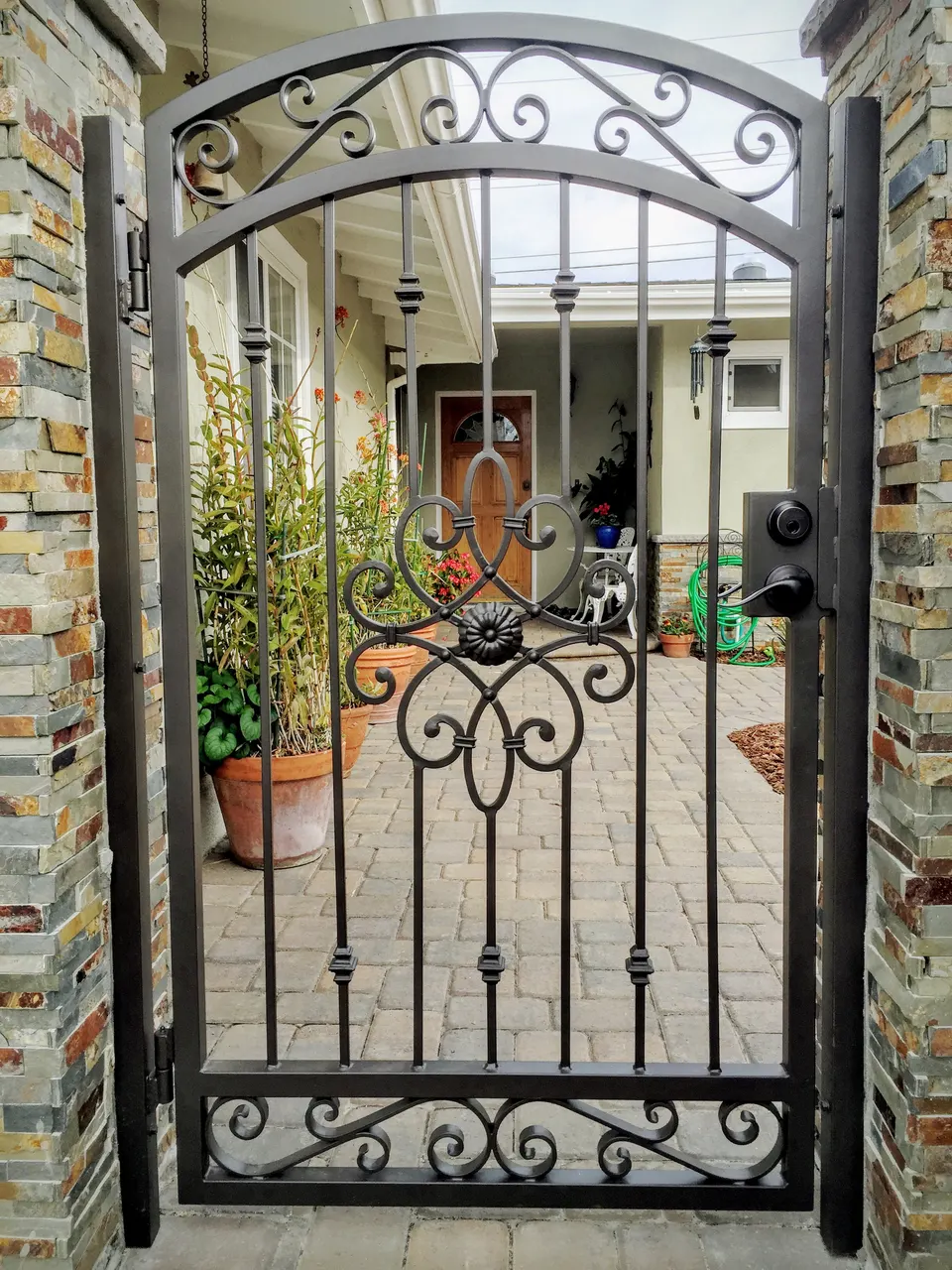 Arched black pedestrian gate with scroll details set between stone-clad posts