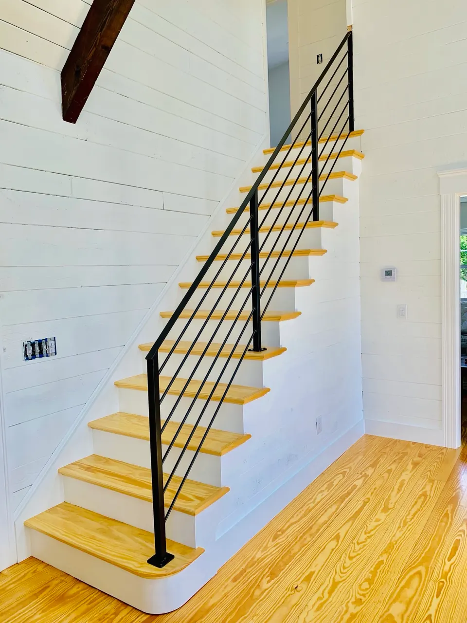 Black railing with horizontal bars beside a wood staircase against a white wall