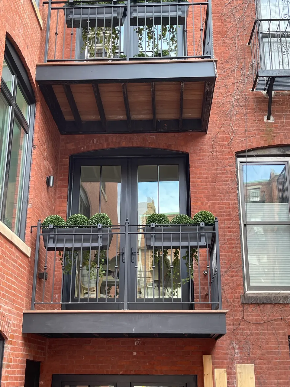 Black steel balcony railing with planter boxes at French doors on a red brick facade