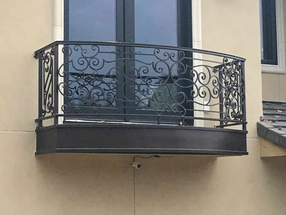 Curved Juliet balcony with scrollwork infill on a tan stucco facade