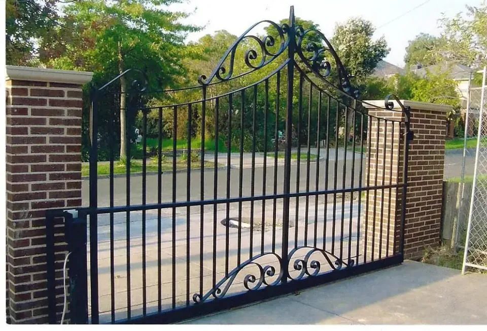 Black ornamental driveway gate between brick piers