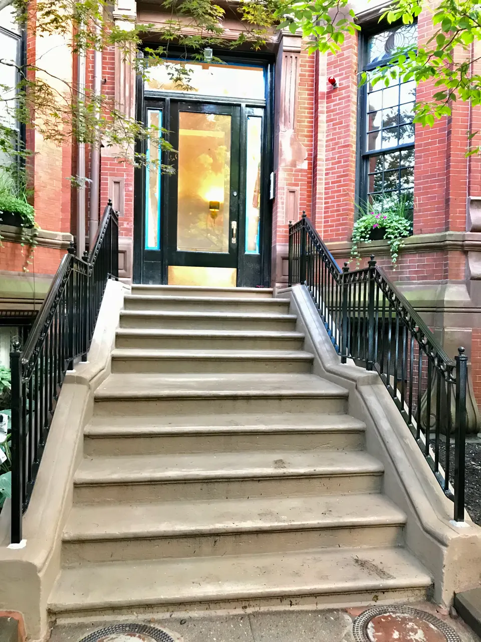 Black picket railings on both sides of wide stone steps leading to a brick townhouse door