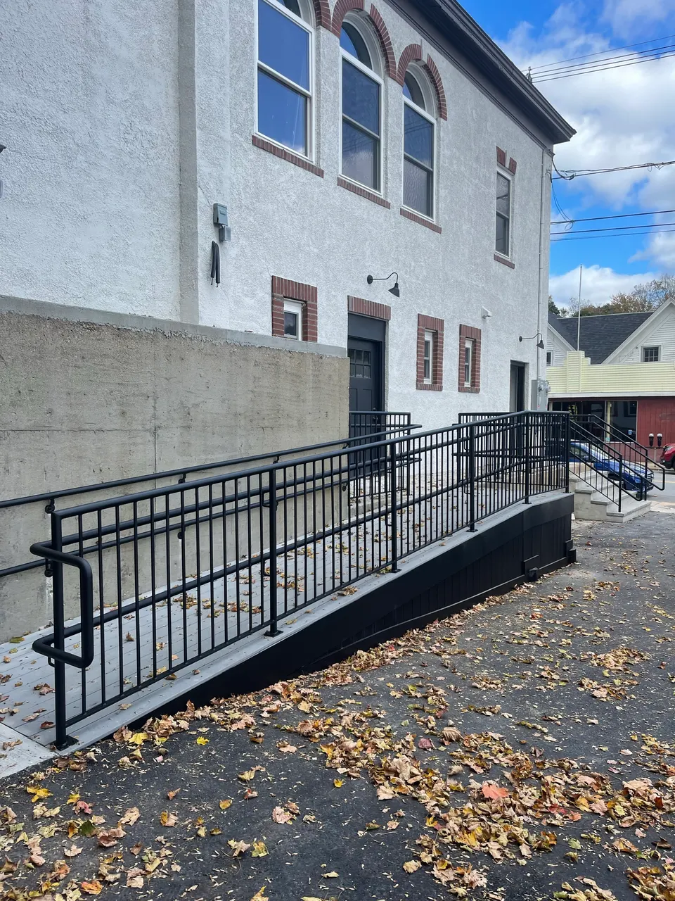 Black ramp railings with a lower handrail beside a stucco building