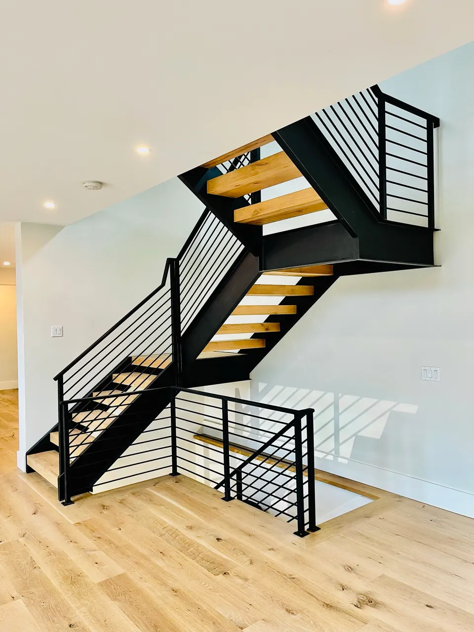 Black steel stair with open wood treads and horizontal-bar railing turning at a landing
