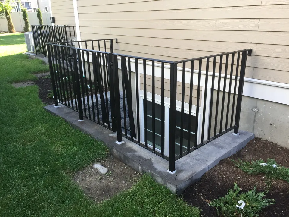Black picket guard rail around a basement window well beside a house